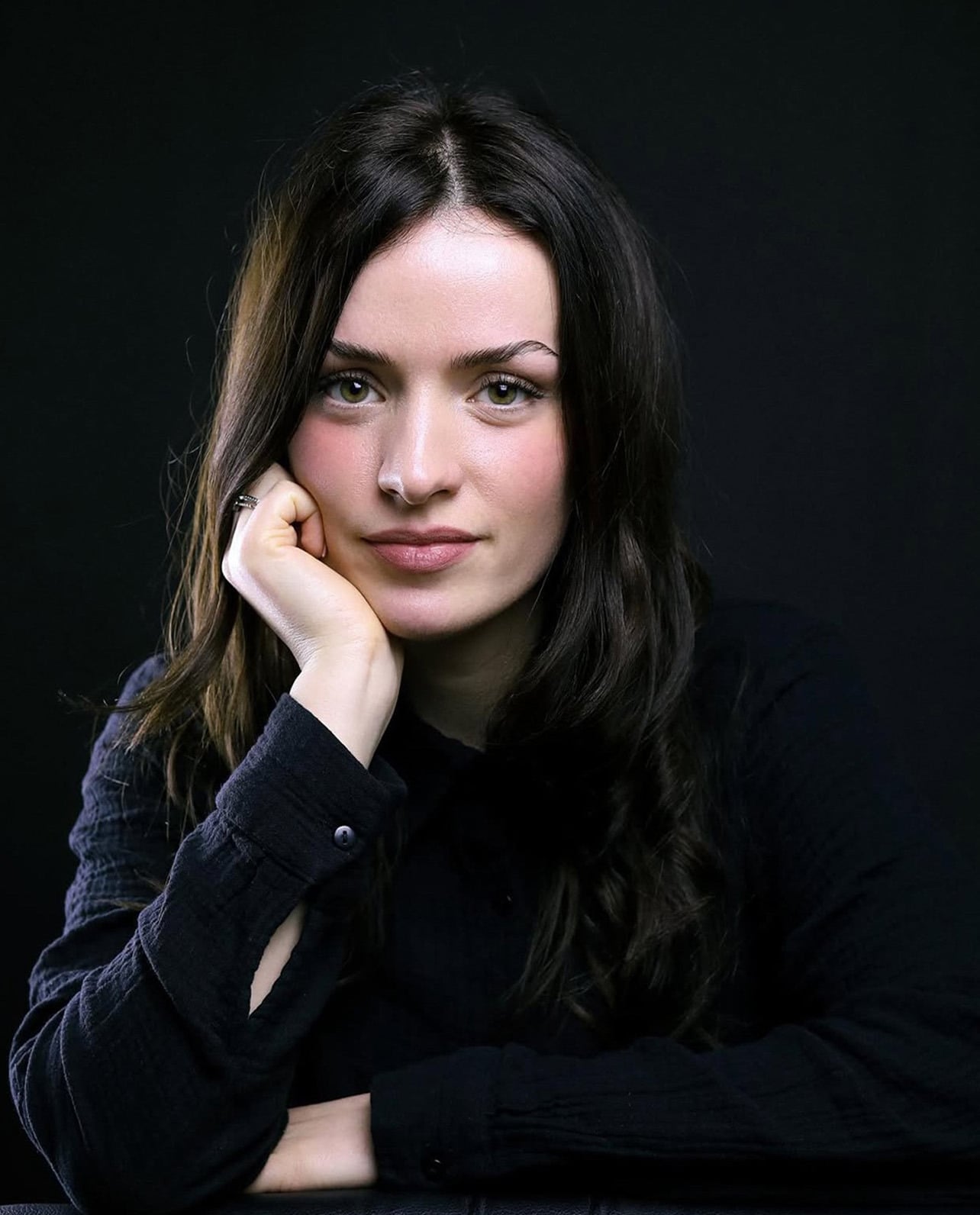 Portrait of Djellza Bajrami against a black background, chin resting on her hand